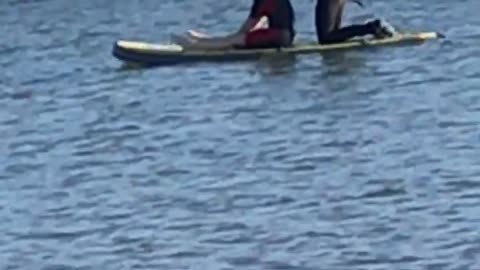 Guy in black wetsuit on surfboard with girl