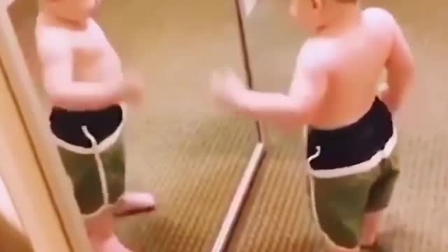 Baby posing like a bodybuilder in front of mirror