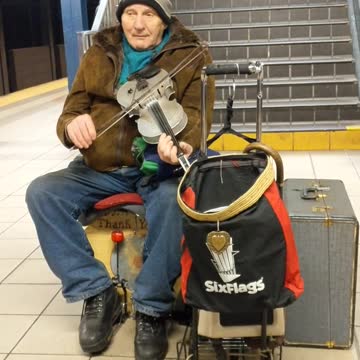 Old man plays violin and cajon box in front of subway escalators