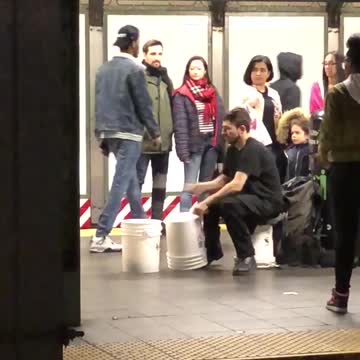 Man in black plays bucket drums