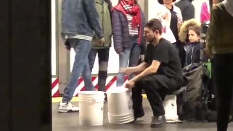 Man in black plays bucket drums