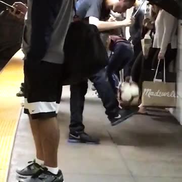 Guy black umbrella subway train station kicking balancing white soccer ball holding green soccer ball