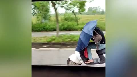 Woman rides scooter with umbrella blocking her view to shield herself from rain in China