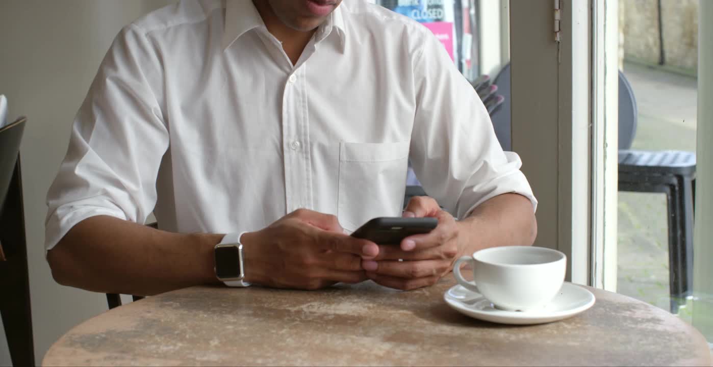 Male customer sitting in cafe using smartphone, mid section