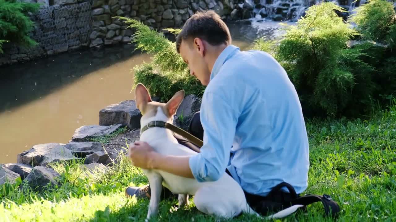 Dog with the owner sit on the banks of a stream with a waterfall