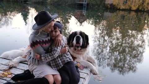 Happy family with their big dog at sunset sit near the lake on an autumn day, enjoying nature