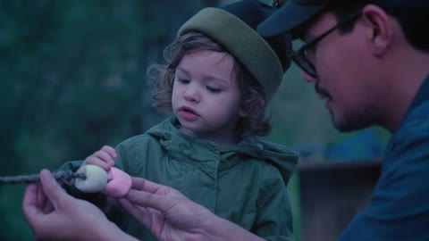 Father and daughter placing marshmallows on a branch outdoors