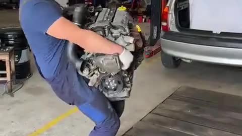 The mechanic installs the car engine.