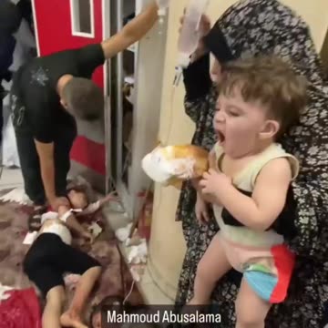 A woman holds an IV bag for a child while holding a baby at Gaza hospital