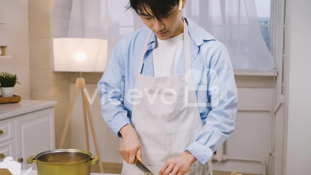 Japanese Man Cutting Ingredients In The Kitchen, Then Looks At The Camera And Smiles 2