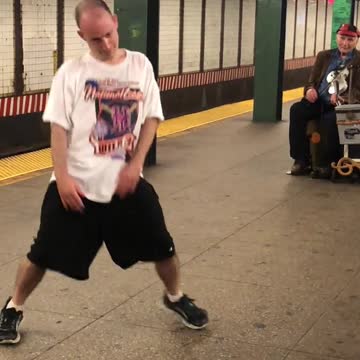 Man in white shirt dances to music from violin in subway station