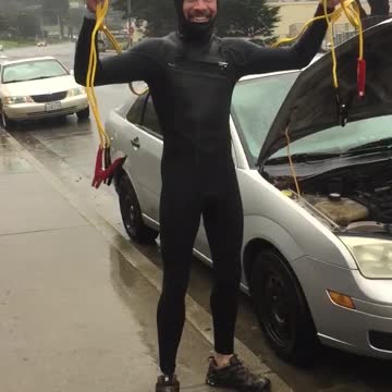 Man in wet suit jumpstarting car
