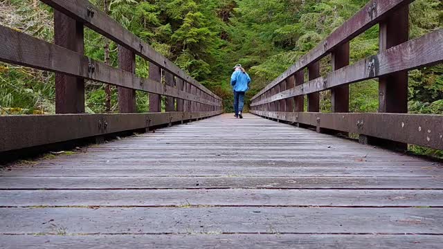 Man Running Away on a Wood Very High Trail Bridge Over a Rushing River.