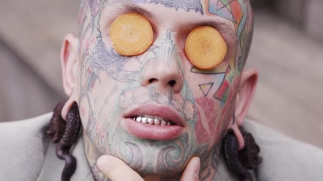 young-tattooed-man-posing-with-carrot-slices-on-eyes