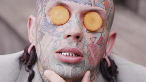 young-tattooed-man-posing-with-carrot-slices-on-eyes