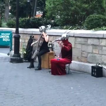 Man on sidewalk floor touching woman's breasts, musicians with metal helmets playing instruments
