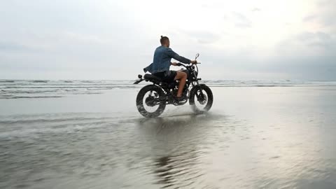 Hipster biker riding a motorcycle near the seashore