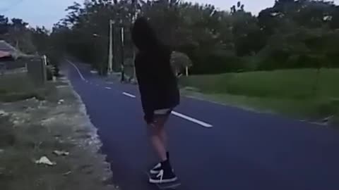 Girl in black sweatshirt and shorts skateboards in front of friend and falls down