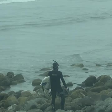 Man scuba gear with surf board walking on rocks