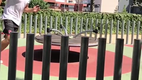 Man with white shirt tries to high jump a bunch of poles on playground in slowmotion but fails and turns ankle
