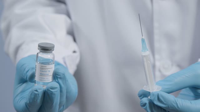 Close Up Shot of Medical Professionals Hand Extracting COVID-19 Vaccine from Vial into a Syringe