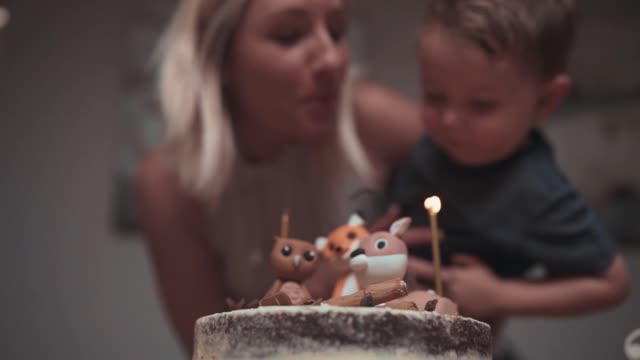 A Mother Helping His Son Blows Off The Candle Flame On His Birthday Cake