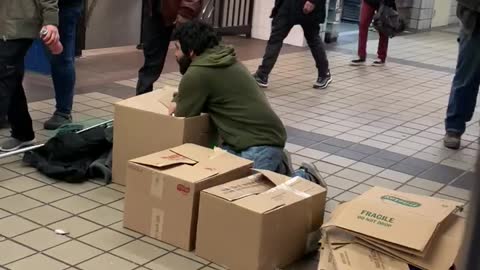 Man organizes things into boxes in the middle of subway station walkway