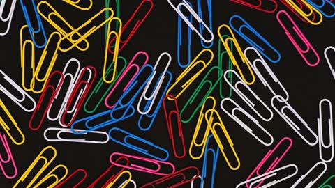 Creative Video of Paper Clips Of Different Colors Moving on a Black Surface