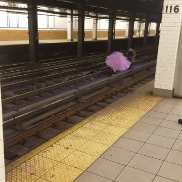 Woman in pink dress dances down subway train tracks