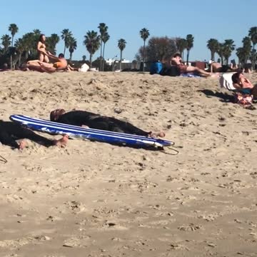 Three guys in wetsuits lay out on the beach