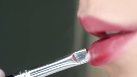 model brushing on red color lipstick on her lips