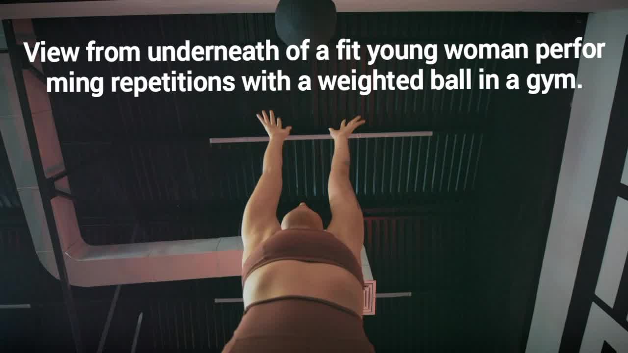 In a gym, a woman is working out with a ball.