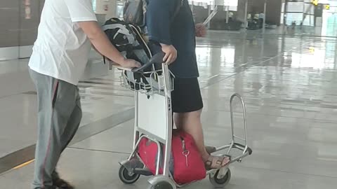 A cute Japanese guy enjoy ride on baggage trolley at airport