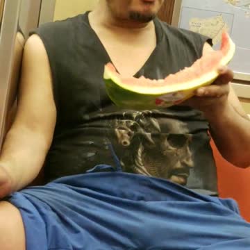 Man on train eating half watermelon