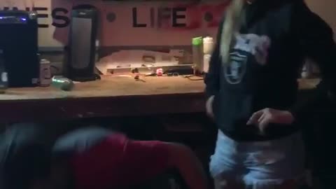 Man in hat kicks can off womans head and it hits dartboard