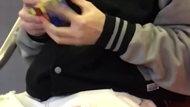 Guy wearing headphones solves a rubik's cube very fast on subway train
