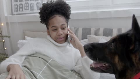 Woman in Bed Talking on the Phone Beside Dog