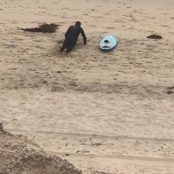 Guy in black wet suit practices blue surfboard