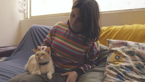 A woman sits on a couch and pets a cat