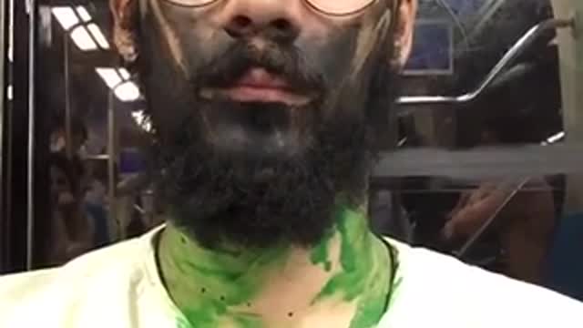 Guy with black and green painted face sits on subway