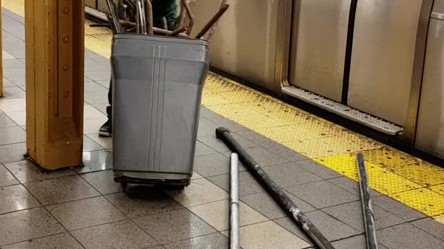 People walking off of subway train with trashcans full of metal and pipes