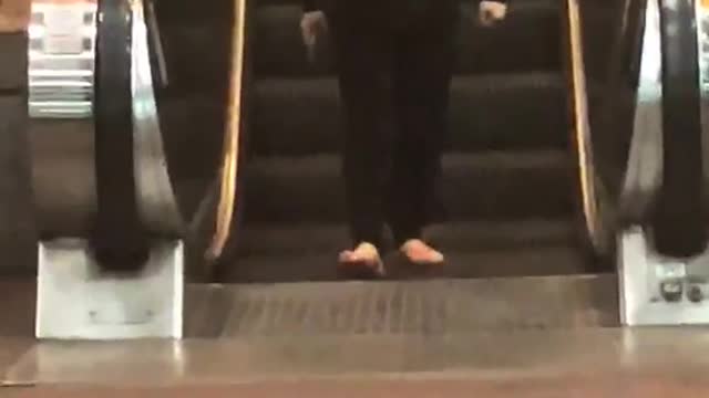 Lady black jacket with hammer and sandals walking backwards escalator