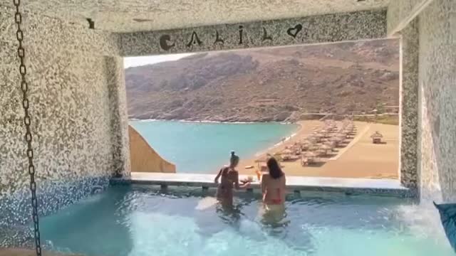 There are two beautiful women playing in the swimming pool by the lake.