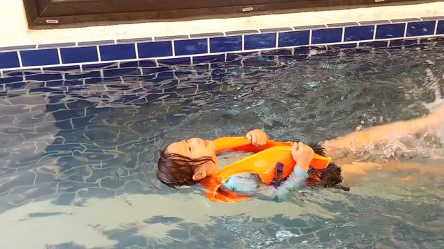 There is a girl swimming in a life jacket.