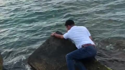 Guy tries to jump on some rocks beach almost slips into water