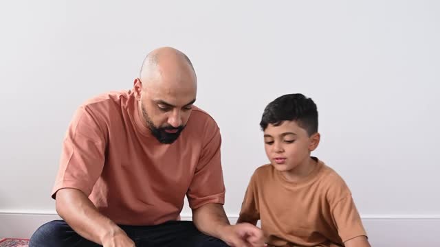 a-man-sitting-on-a-carpet-with-his-son-while-browsing-a-quran-book