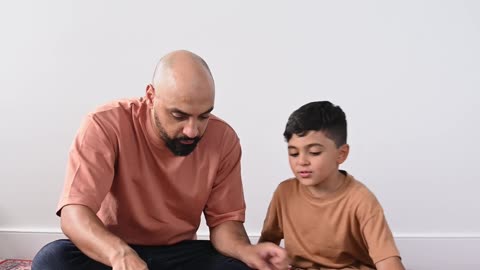 a-man-sitting-on-a-carpet-with-his-son-while-browsing-a-quran-book