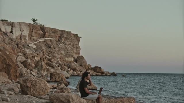 Man Working Remotely by the Beach and Using a Mobile Phone