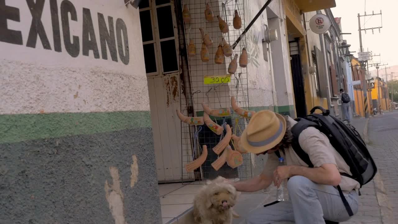 a backpack and a hat petting a stray dog next to a Mexicano sign in Mexico