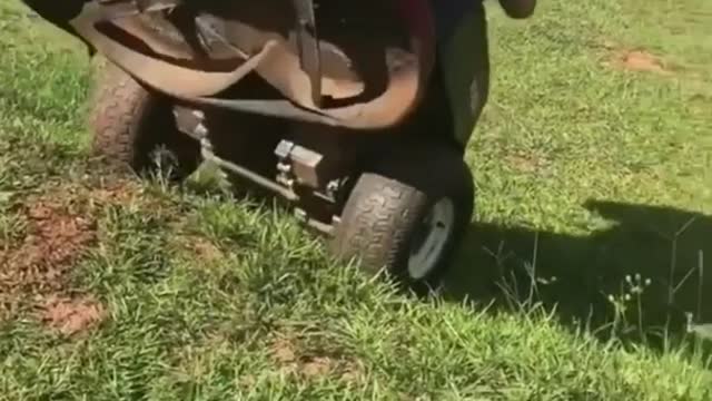 Kid drives red lawnmower up hill and it topples on top of him